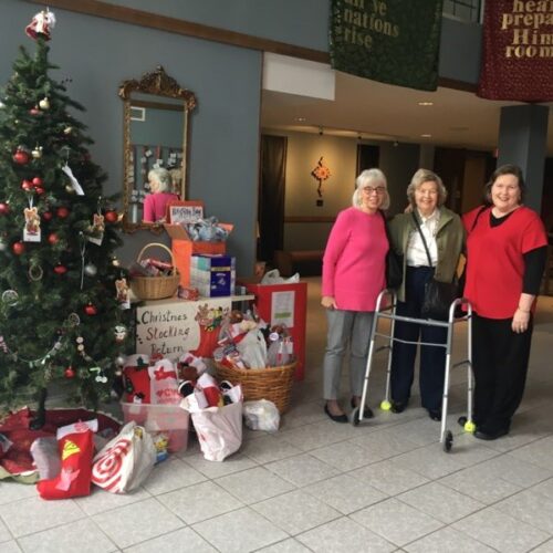 Highland Park members stand by Christmas Stocking donations in the atrium
