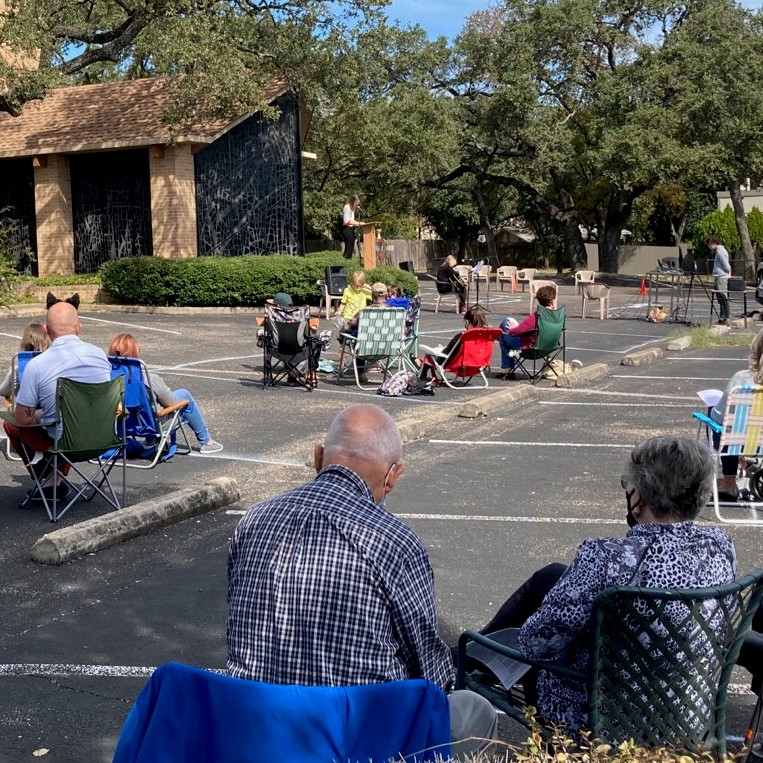 Worshippers sit outdoors as staff leads outdoor worship