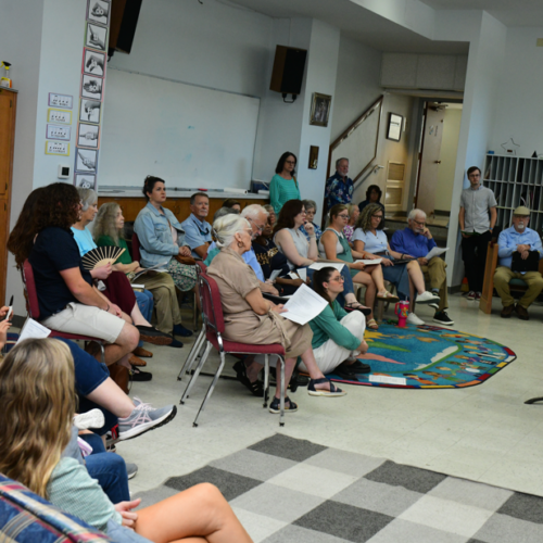 The congregation sits in chairs, couches, and on the ground as they listen to rev cheryl kimble preach